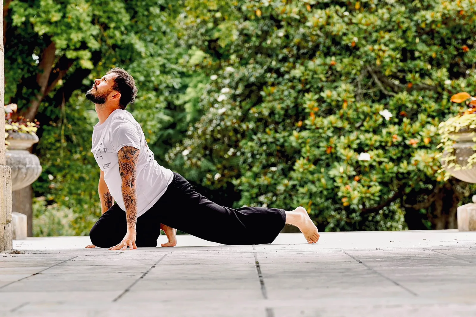 Baptiste Honorez en posture de Qi Gong, à quatre pattes, dos cambré et regard levé, dans un parc